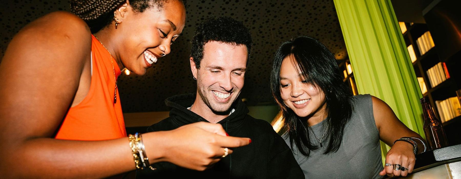 A group of people smiling and looking at a cell phone.